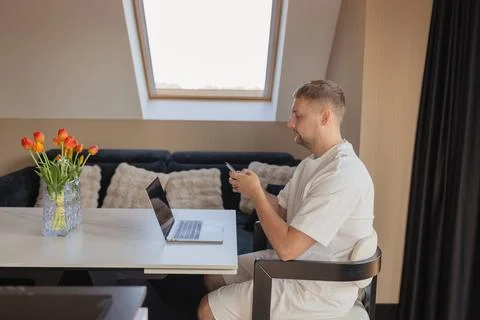 Man using smartphone while working with laptop at home office. Concept of remote Stock Photos
