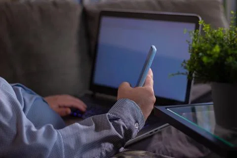 Man using smartphone while working on laptop sitting on couch 写真素材