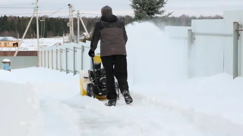 Man using snow plow machine to clear his backyard, rear view. SM 120fps Stock Footage 296799048