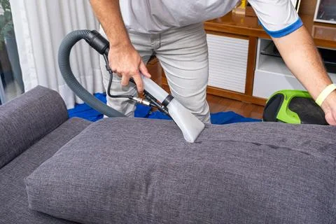 Man using a special vacuum to clean gray sofa cushions side view. Stock Photos
