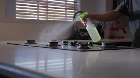 Man using spray bottle to spray soapy water on stove top to clean Stock Footage 284215698