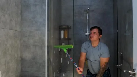 Man using a squeegee to clean glass shower wall, removing water drops and soap Video stock 333579940