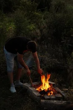 A man is using a stick in the process of lighting a fire Foto stock