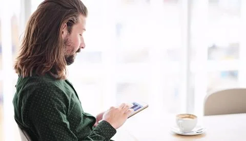 Man using tablet in cafe while seated next to window Stock Photos