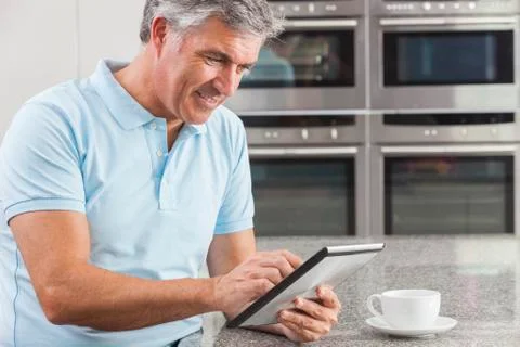 Man using tablet computer in kitchen drinking coffee Stock Photos