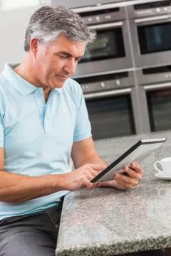 Man using tablet computer in kitchen drinking coffee Stock Photos