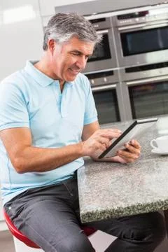 Man using tablet computer in kitchen drinking coffee Stock Photos