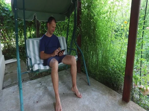 Man using tablet computer touchscreen sitting on the swing relax and smiling Video stock 72568472