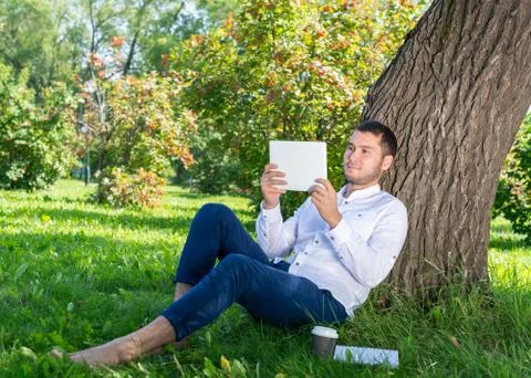 Man using tablet computer under tree in park Stock Photos