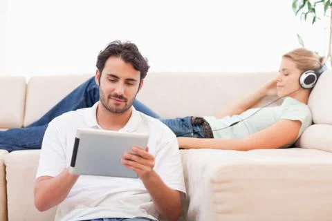 Man using a tablet computer while his girlfriend is listening to music Stock Photos