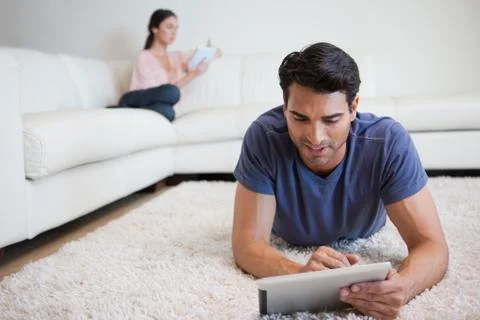 Man using a tablet computer while his girlfriend is reading a book Stock Photos