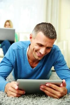 Man using a tablet computer while his girlfriend using laptop at home 写真素材