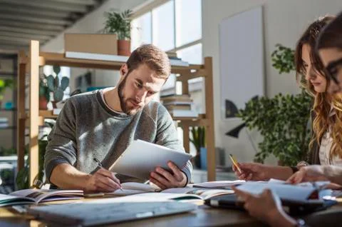 Man using tablet computer while studying with friends at table in classroom Stock Photos