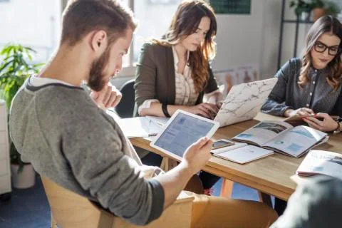 Man using tablet computer while studying with friends at table in classroom Stock Photos