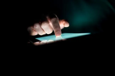 Man using a tablet in the dark navigating the glowing blue touchscreen with.. Foto stock