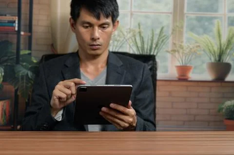 Man Using a Tablet at a Desk in a Bright, Home Office with Plants Stock Photos