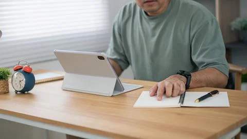 Man using tablet with foldable cover and writing notes in notebook at woode.. Stock Photos