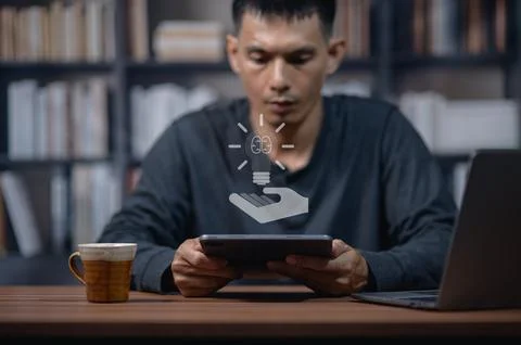 Man using tablet in library with glowing light bulb icon and digital interfac Stock Photos