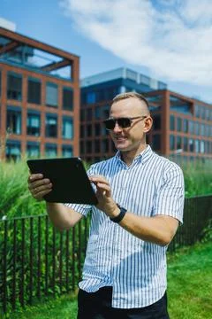 Man using tablet in outdoor area near modern buildings in bright daylight Stock Photos