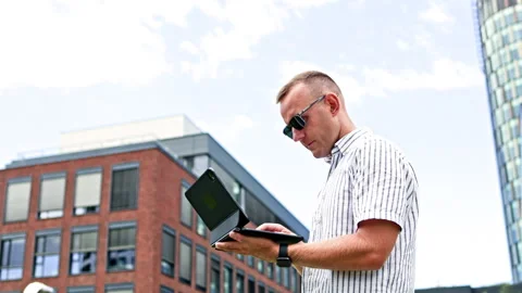 Man using a tablet outdoors in front of brick offices and a glass tower during Stock Footage 348703279