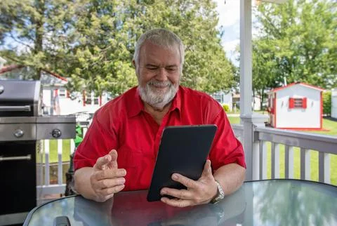 Man Using Tablet Outside During a Sunny Day in a Backyard Setting With Greene Foto stock