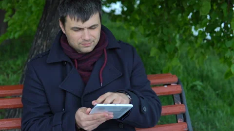 The man is using a tablet in the park. Stock Footage 91127306