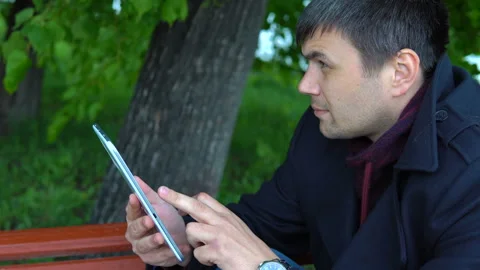 The man is using a tablet in the park. Stock Footage 91129367