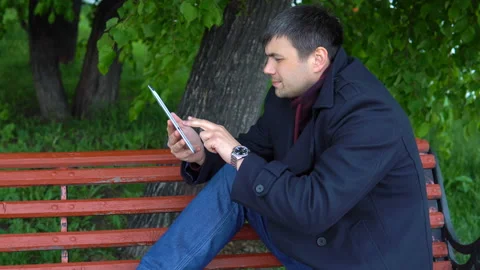 The man is using a tablet in the park. Video stock 91130934