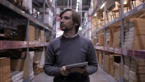 Man using tablet pc against shelves with boxes in warehouse. Handsome Stock Footage 72026533