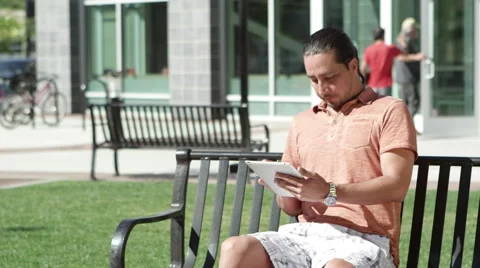 Man using tablet sitting on park bench Stock Footage 67364731