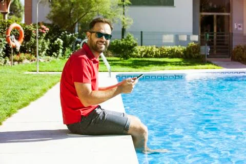 Man using tablet sitting on the poolside. Stock Photos