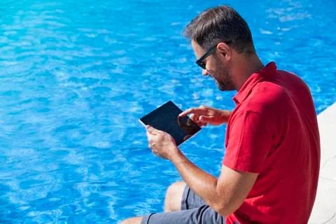 Man using tablet sitting on the poolside. Stock Photos