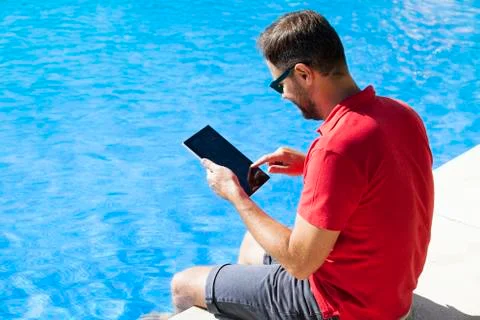 Man using tablet sitting on the poolside. Stock Photos