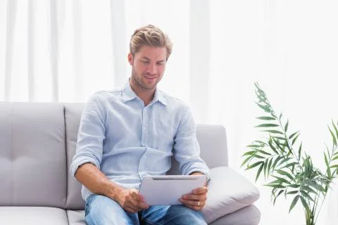Man using a tablet while he is sat on the couch Stock Photos
