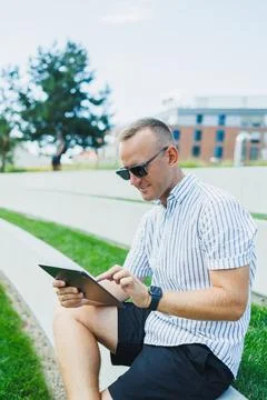 Man using a tablet while sitting on steps in a park during daytime Stock Photos