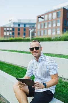 Man using tablet while sitting on concrete steps in an urban area on a sunn.. Stock Photos