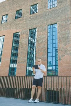 Man using a tablet while standing near a brick building with large windows .. Stock Photos