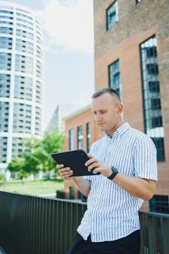 Man using a tablet while standing on a balcony in a city with modern buildi.. Stock Photos