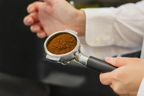 Man is using a tamper to press freshly ground morning coffee into a coffee ta Stock Photos