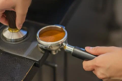 Man is using a tamper to press freshly ground morning coffee into a coffee ta Stock Photos