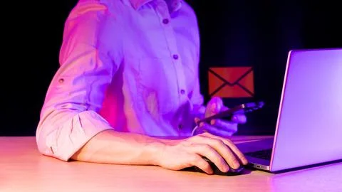 Man using tech gadgets with holographic envelope icon in purple lighting 写真素材