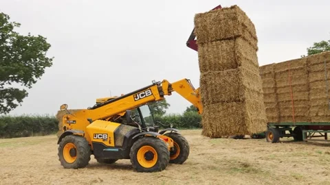 Man using a telehandler to load bales of straw onto a tractor trailer. UK Stock Footage 160260658