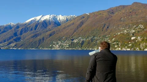 Man Using a Telescope to Looking at Alpine Lake with Snow-capped Mountain Stock Footage 164712987