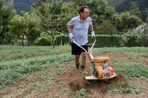 Man using tiller in vegetable garden Stock Photos