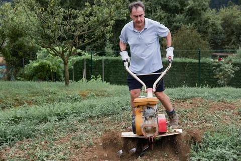 Man using tiller in vegetable garden Foto stock