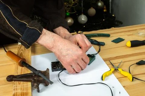 A man is using a tool to fix the wiring of a Christmas tree garland. Tools .. Stock Photos