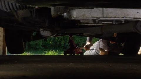 A man using a trolley jack in a garage to lift a vehicle off the ground. Stock Footage 278025782