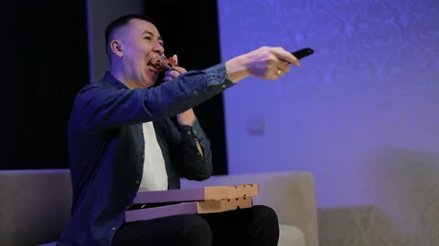 Man using tv remote for changing channel while eating pizza. Focused young man Stock Footage 194548645
