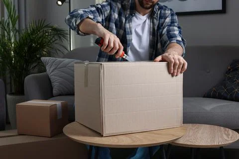 Man using utility knife to open parcel at home, closeup Stock Photos
