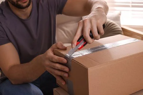 Man using utility knife to open parcel at home, closeup Stock Photos